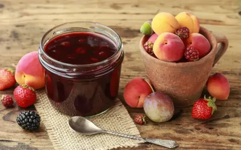 Ein Glas selbstgemachte Marmelade mit frischen Früchten daneben. Die Frage "wie lange ist selbstgemachte Marmelade haltbar" beschäftigt viele Hobbyköche.