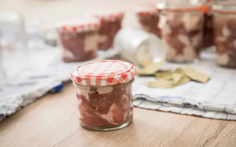 Słoiki z mięsem, przygotowane do tyndalizacji. Na stole leżą też liście laurowe.