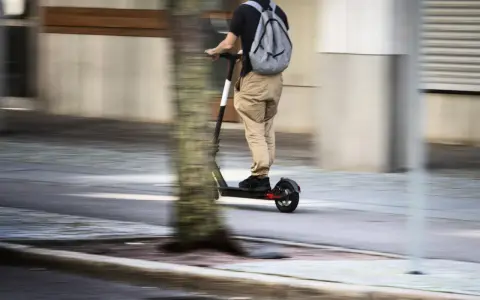 En person på elsparkcykel, med ryggsäck, susar fram på trottoaren. Frågan om får man åka två på elsparkcykel är relevant här.