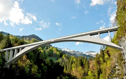 El puente de Salginatobel se alza majestuoso sobre un valle verde, con picos nevados al fondo.