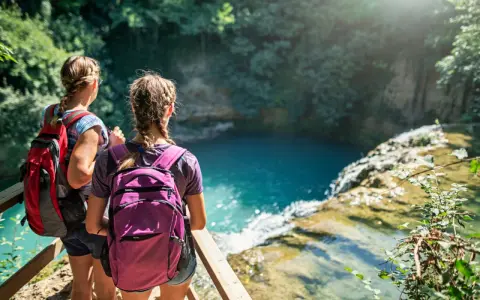 Due escursioniste con zaini ammirano una cascata turchese durante il loro trekking in Toscana.