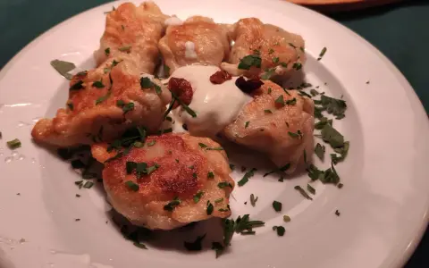 Pierogi, un piatto tipico polacco, serviti su un piatto bianco con panna acida e prezzemolo tritato.