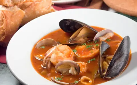 Sopa de mariscos en plato blanco con mejillones, camarones, almejas y pan.