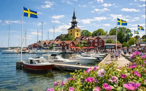 En livlig hamn med svenska flaggor, båtar och röda hus. Kanske en vy från ett mysigt hotell i Norrbotten en solig sommardag.