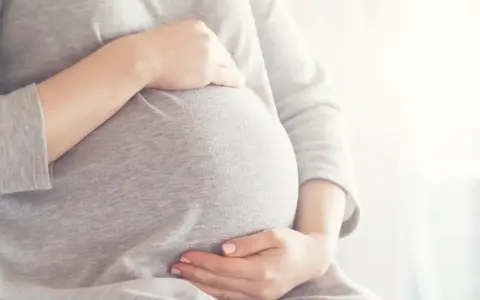 Brzuszek w 6 miesiącu ciąży, delikatnie otulony dłońmi.
