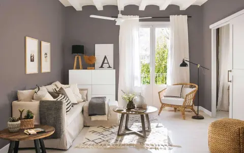 Salones pequeños con encanto: un sofá beige, sillón de mimbre, mesas de madera y detalles decorativos crean un espacio acogedor.