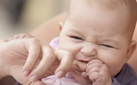 Ein süßes Baby mit einem lustigen Gesichtsausdruck, das gerade versucht, den Finger einer erwachsenen Person zu beißen.