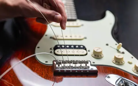 Dłoń naciąga nowe struny w gitarze elektrycznej, przygotowując ją do gry.