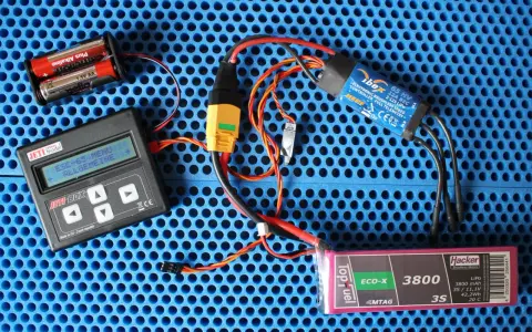 Jeti Box mit ESC-65-Menü, ibex 65 HV ESC, Hacker LiPo-Akku und Batterien auf blauem Untergrund.