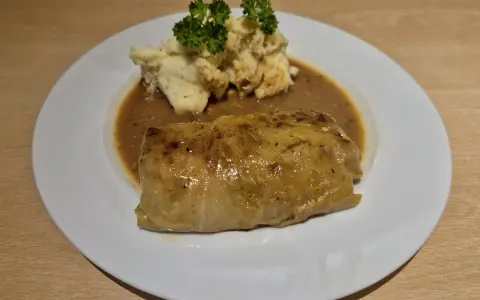 Ein herzhaftes Krautwickel Rezept auf einem Teller mit Kartoffelbrei und Sauce, garniert mit Petersilie.