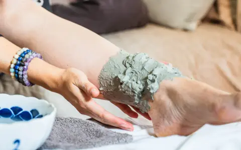 Application d'un cataplasme d'argile verte sur une jambe, pour un soin détoxifiant et apaisant.