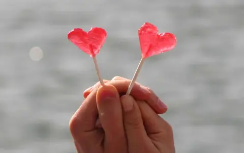 Dos piruletas rojas en forma de corazón, sostenidas por manos entrelazadas, como un símbolo de amor y una **venus carta astral**.