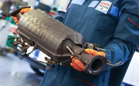 Mechanik w rękawiczkach trzyma zużyty katalizator, prawdopodobnie z Peugeota p2448.