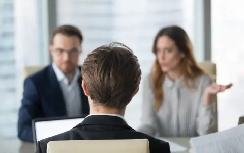 Besprechung mit einem Anwalt über Versicherungsansprüche. Eine Frau gestikuliert, während ein Mann mit Brille und ein Mann im Vordergrund zuhören.