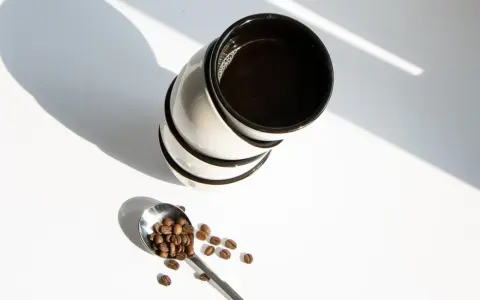 Stos kawy w filiżankach i łyżka z ziarnami kawy. Zastanawiasz się, ile kofeiny ma kawa w 100 ml?
