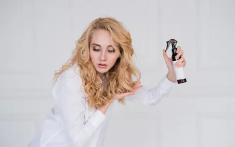 Blondynka z pięknymi, naturalnymi falami na włosach testuje nowy spray do stylizacji.