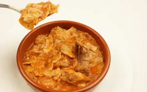 Un plato humeante de comida típica de Albacete, con trozos de carne y pasta en una salsa rojiza.