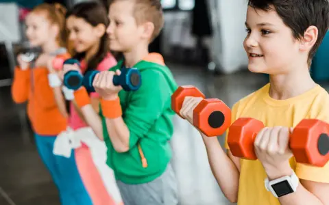 Dzieci ćwiczą z hantlami podczas zajęć si. Uśmiechnięci mali sportowcy budują siłę.