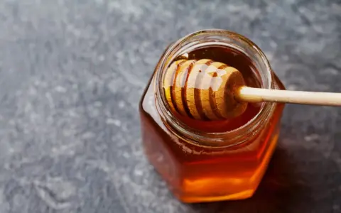 Ein Glas mit flüssigem Honig und einem Honigheber. Dieser goldene Nektar ist nicht nur lecker, sondern auch honig gesund.