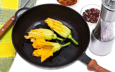 Fiori di zucca in padella, pronti per essere impanati e fritti. Accanto, spezie e sale per insaporire.