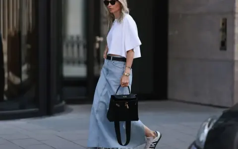 Kobieta w białej bluzce i długiej spódnicy jeansowej, z czarną torebką i sneakersami. Stylowe długa spódnica jeansowa stylizacje.