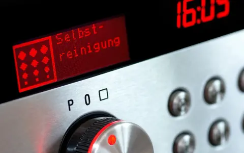 Bedienfeld eines Ofens mit rotem Display, das "Selbst-reinigung" anzeigt. Daneben die Uhrzeit 16:05.
