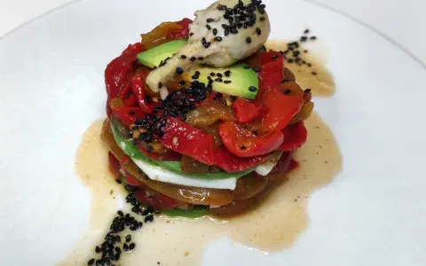 Torre de pimientos del piquillo asados, aguacate y queso fresco, coronada con un alcachofa y semillas de sésamo negro.