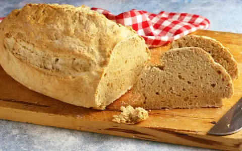 Pane casereccio con lievito istantaneo, tagliato su un tagliere di legno, con un tovagliolo a quadri rossi e bianchi.
