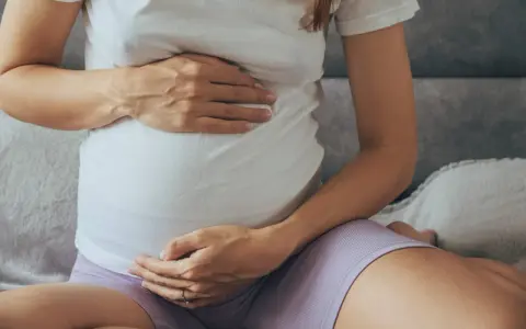 Brzuch kobiety w ciąży, z dłońmi delikatnie go obejmującymi.