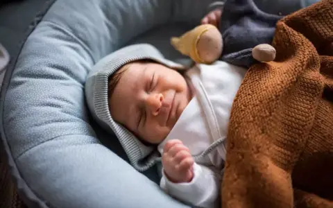 Ein Neugeborenes schläft friedlich in einer Babywippe, eingewickelt in eine warme Decke. Vielleicht ist es der 37 wochen schub, der ihm süße Träume schenkt.