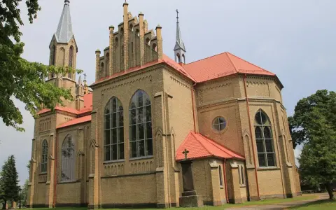 Gotycka ceglana świątynia z czerwonym dachem, jedna z krynki atrakcje. Wokół drzewa i trawnik.