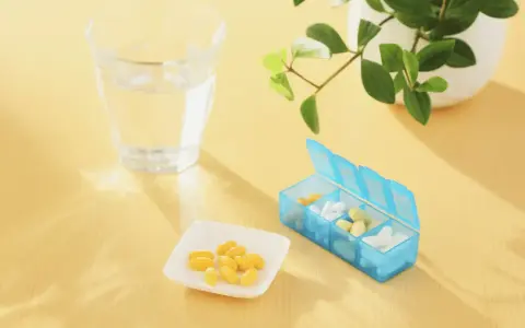 Un bicchiere d'acqua, una ciotolina con capsule gialle e un portapillole blu. Forse integratori per capire cosa sono gli elettroliti.