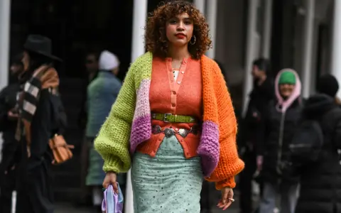 Bunte Strickjacke mit Ballonärmeln, die zeigt, wie man einen Cardigan kombinieren Damen kann. Dazu ein mintgrüner Rock und auffälliger Gürtel.