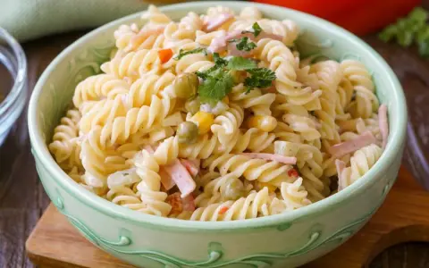 Ein cremiger Nudelsalat mit Erbsen, Mais und Schinkenwürfeln, der an einen herzhaften Fleischsalat erinnert. Garniert mit Petersilie.