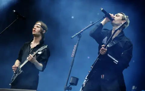 Gustaf Norén sjunger och spelar gitarr med Mando Diao på scenen, omgiven av rök och blått ljus.