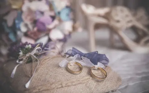 Anillos de boda sobre cojín rústico, ideas para decorar la habitación donde se viste la novia con flores y zapatos elegantes.