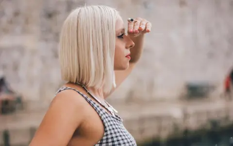 Frau mit blondem **long bob naturwelle** blickt in die Ferne, die Hand schützend über die Augen gelegt.