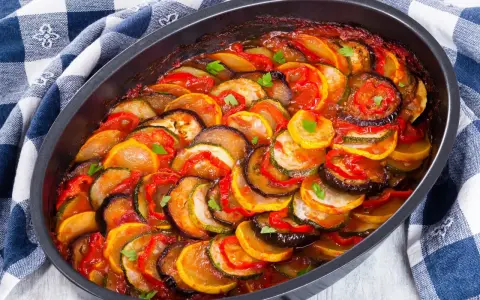 Gotowy ratatouille przepis w naczyniu żaroodpornym, z plasterkami cukinii, bakłażana i pomidorów, polany sosem.