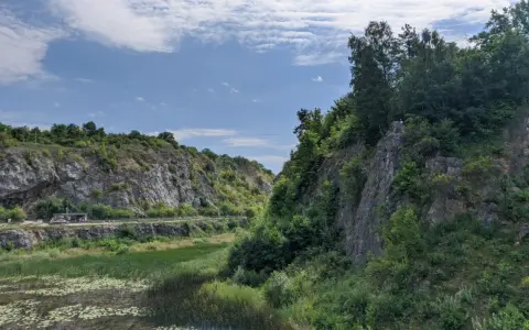 Kamieniołom z wodą i zielenią, skalne zbocza, niebo z chmurami.