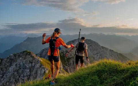 Dwie osoby w sportowym stroju, z plecakami i kijkami, biegną po górskim szlaku. Idealny przykład, jak się ubrać w góry na bieg.