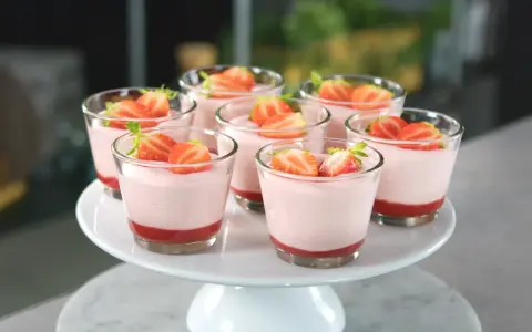 Deliziosi dolci al cucchiaio alla fragola, serviti in bicchierini trasparenti e guarniti con fragole fresche.