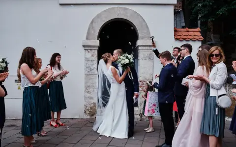 Para młoda całuje się przed kościołem, goście sypią bańki mydlane. To piękny ślub jednostronny, pełen radości i miłości.