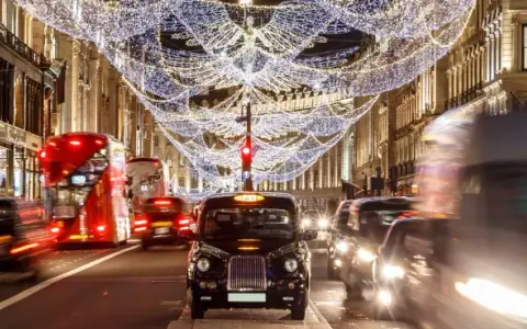 Julbelysning i London i december. Röda dubbeldäckare och taxibilar susar förbi på en livlig gata.