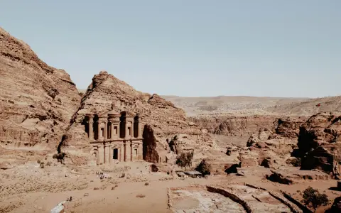 The ancient jordan ruins of Petra, carved into sandstone cliffs, stand majestically under a clear blue sky.