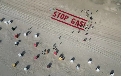 Menschen bilden auf einem Strand "STOP GAS!" als Zeichen für Deutschland klimaneutral. Viele Strandkörbe sind zu sehen.