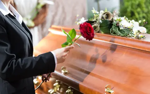 Eine Frau in Trauer legt eine rote Rose auf den Sarg. Sie muss die Beerdigung ihres getrennt lebenden Ehemanns bezahlen.