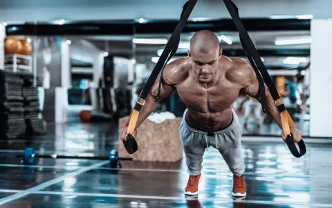 Hombre musculoso realizando trx ejercicios en un gimnasio, con el cuerpo tenso y sudoroso.
