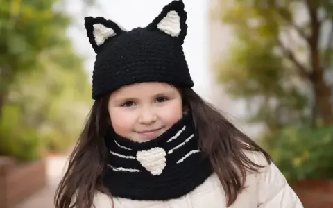 Niña sonriente con un gorro de lana con orejas de gato y bufanda a juego, tejida con agujas.