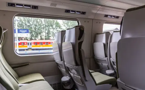 Wnętrze wagonu bez przedziałów IC. Rozkład miejsc z zielonymi siedzeniami i stolikami. Za oknem peron i pociąg.