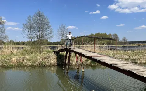 Osoba z rowerem na drewnianym mostku nad rzeką. Piękny dzień na odkrywanie tras rowerowych łódzkiego.